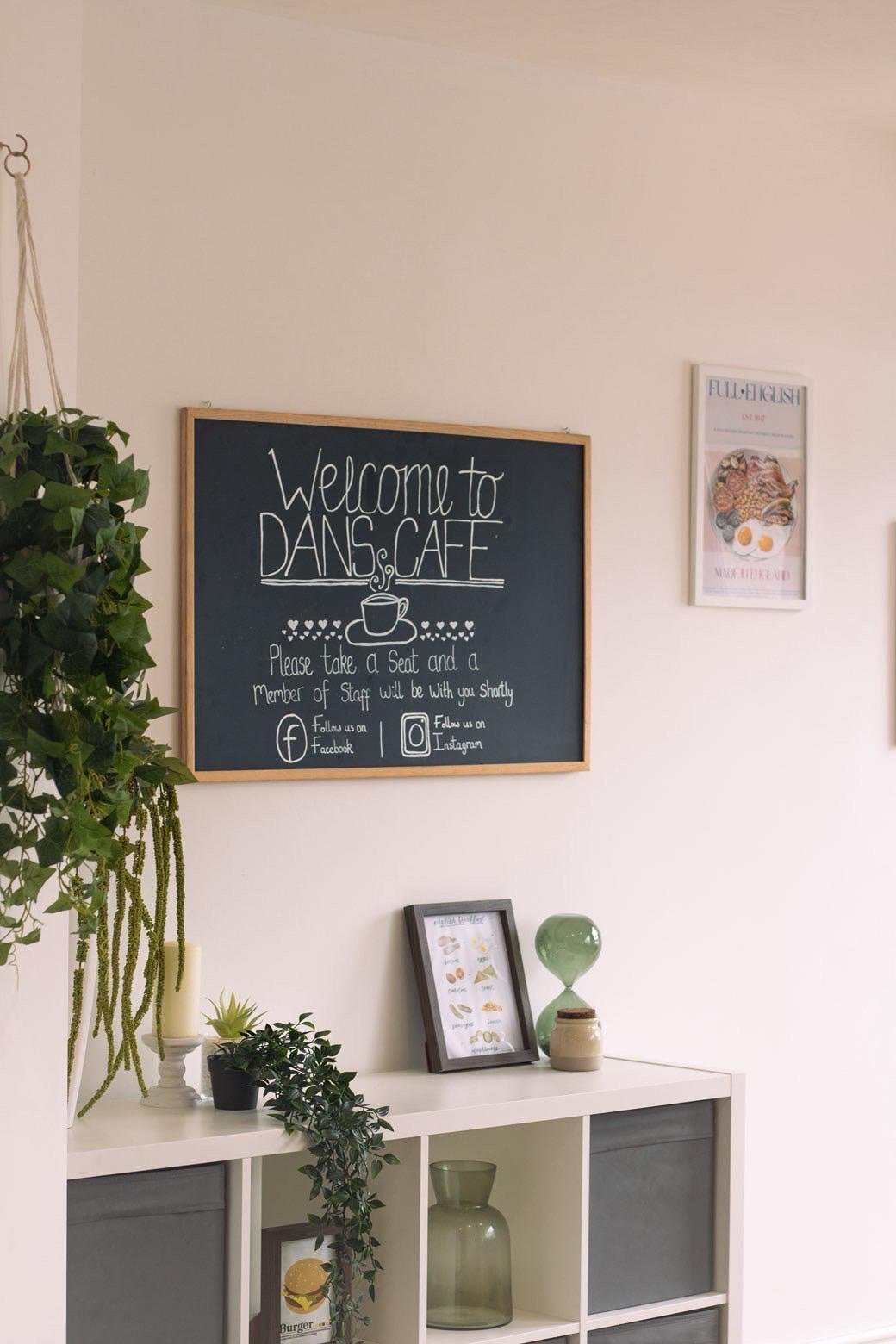 A chalkboard reading 'Welcome to Dan's Cafe' beside hanging plants