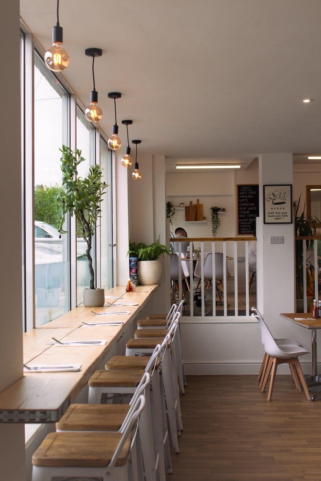 Inside Dan's Cafe — window bar seating with hanging Edison bulbs and plants